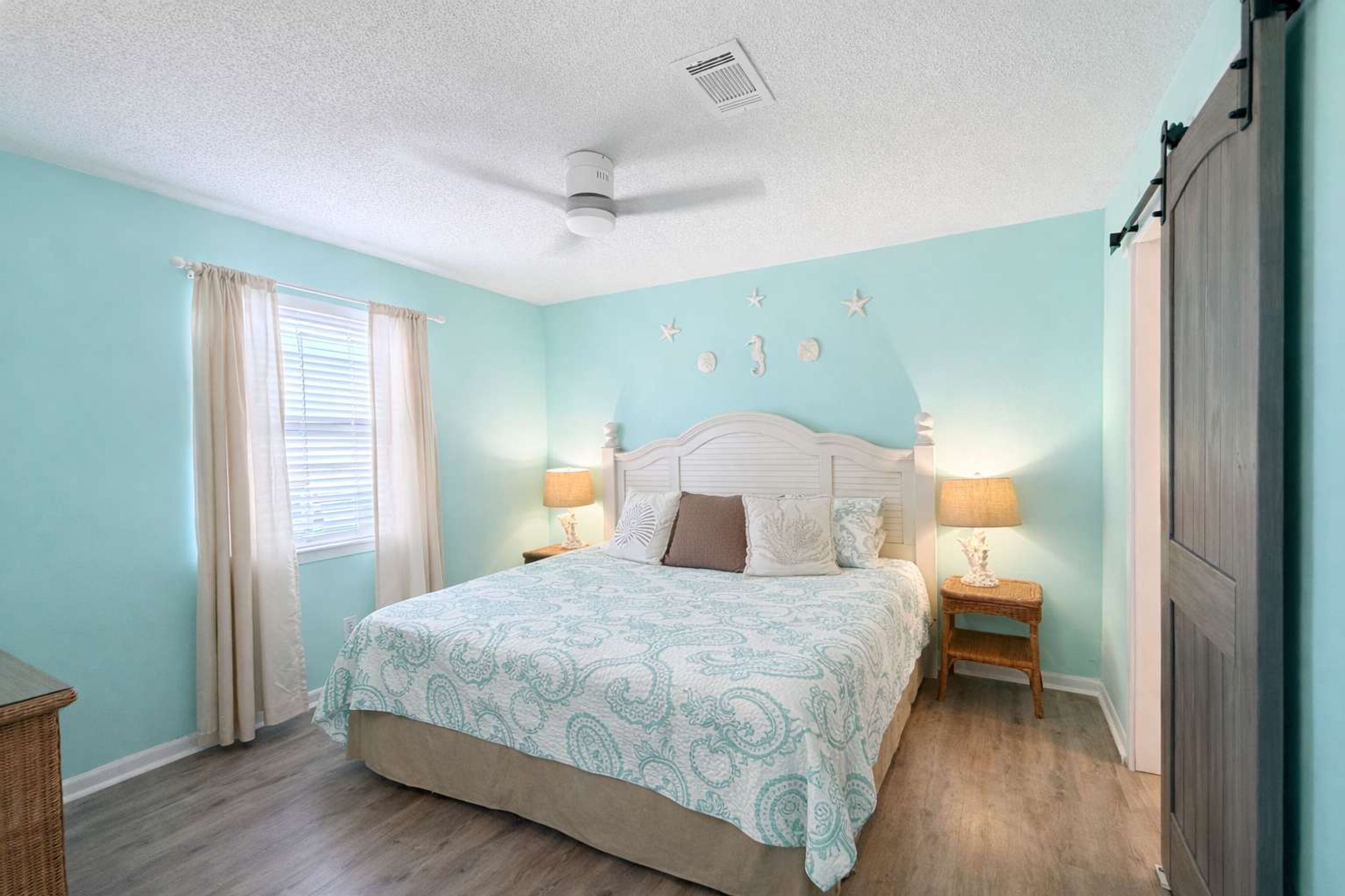 A bedroom with a bed, two bedside tables, a ceiling fan, and a window with curtains.