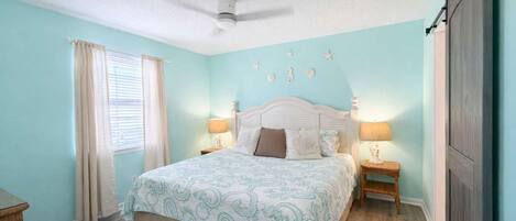 A bedroom with a bed, two bedside tables, a ceiling fan, and a window with curtains.