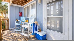 Un portico coperto con pavimento in legno, poltrone Adirondack bianche e blu, un contenitore frigo blu e un estintore rosso.