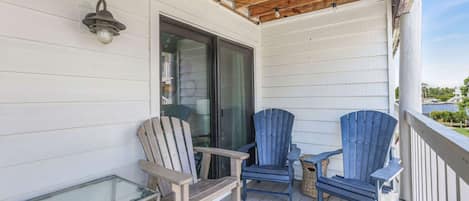 A wooden deck with two Adirondack chairs and a glass table.