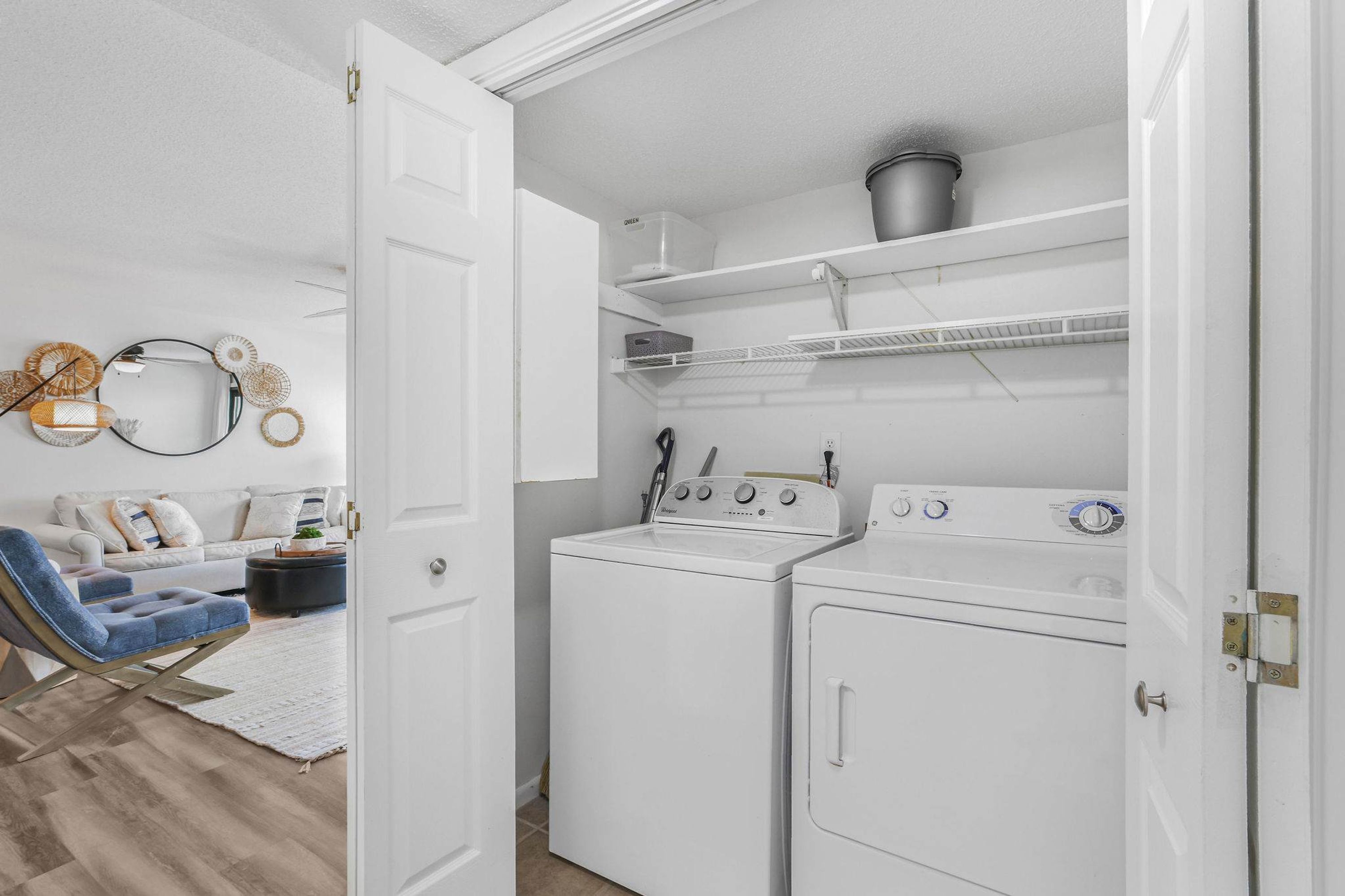 A laundry room with a washing machine and dryer, a white door, and a shelf with a pot.