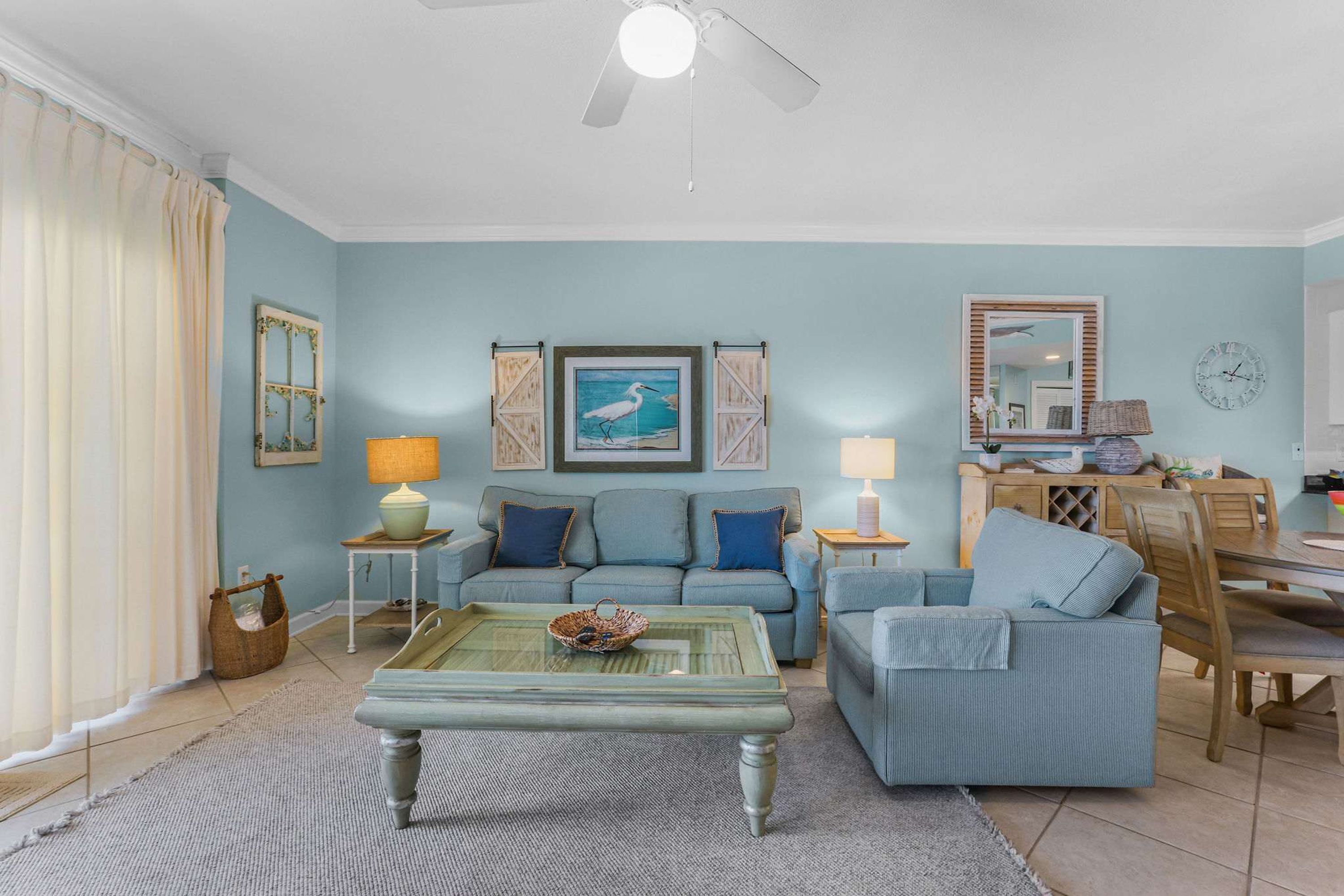 A living room with a blue sofa, a glass coffee table, and a dining area with a wooden table and chairs.
