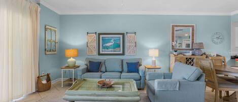 A living room with a blue sofa, a glass coffee table, and a dining area with a wooden table and chairs.