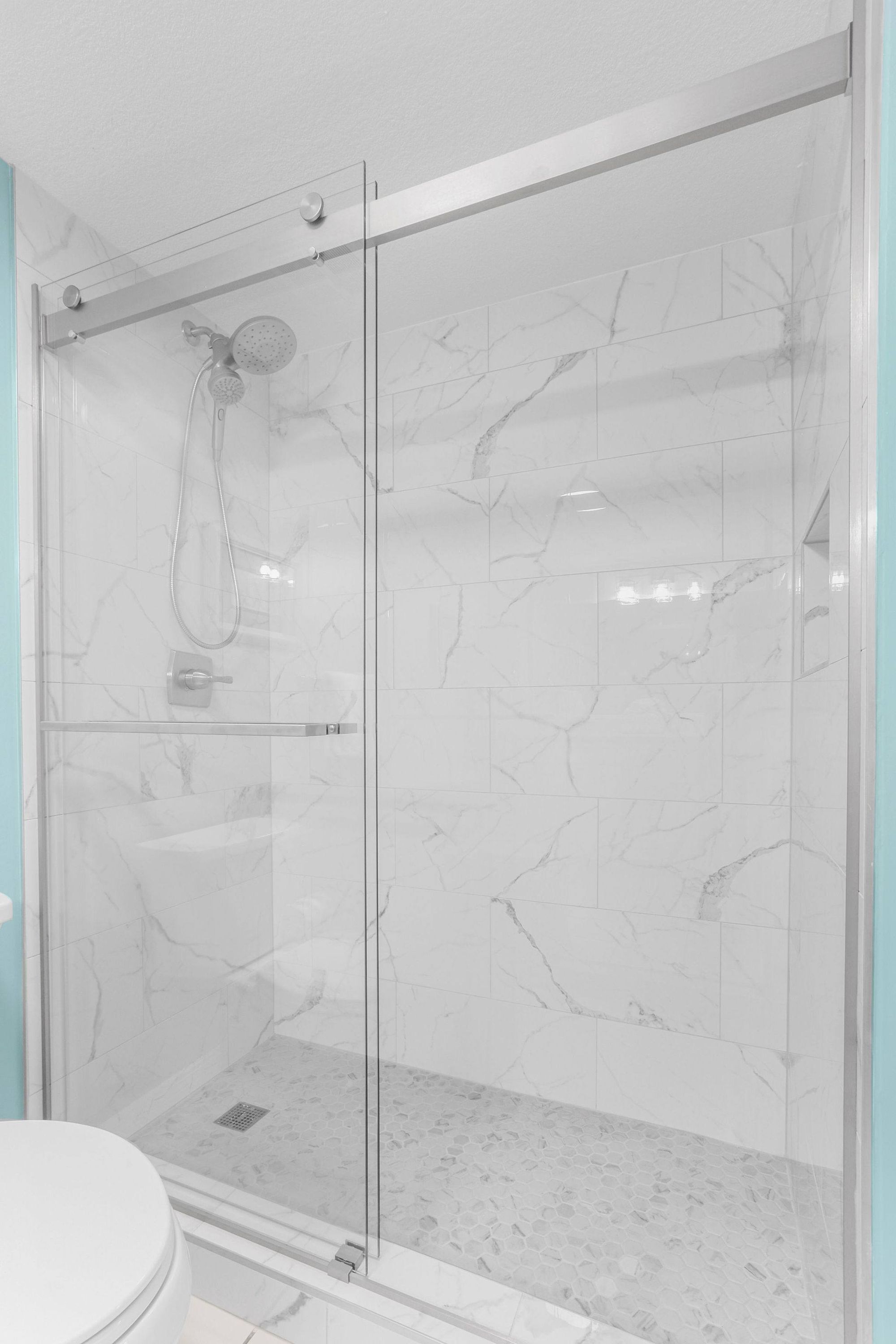 A glass-enclosed shower area with a marble floor and a white toilet visible to the left.
