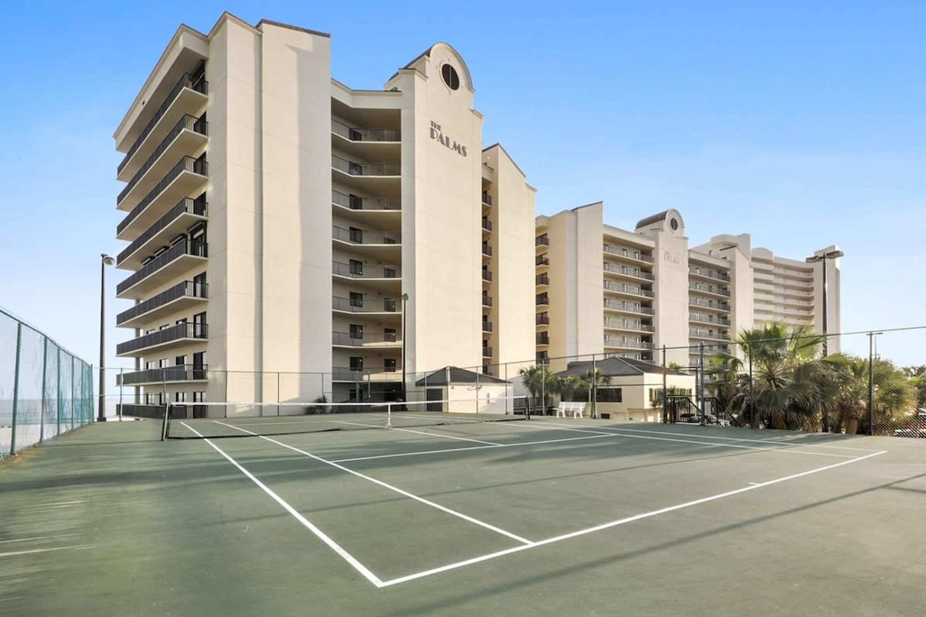 Un hotel con varios pisos, cancha de tenis y zona de piscina.