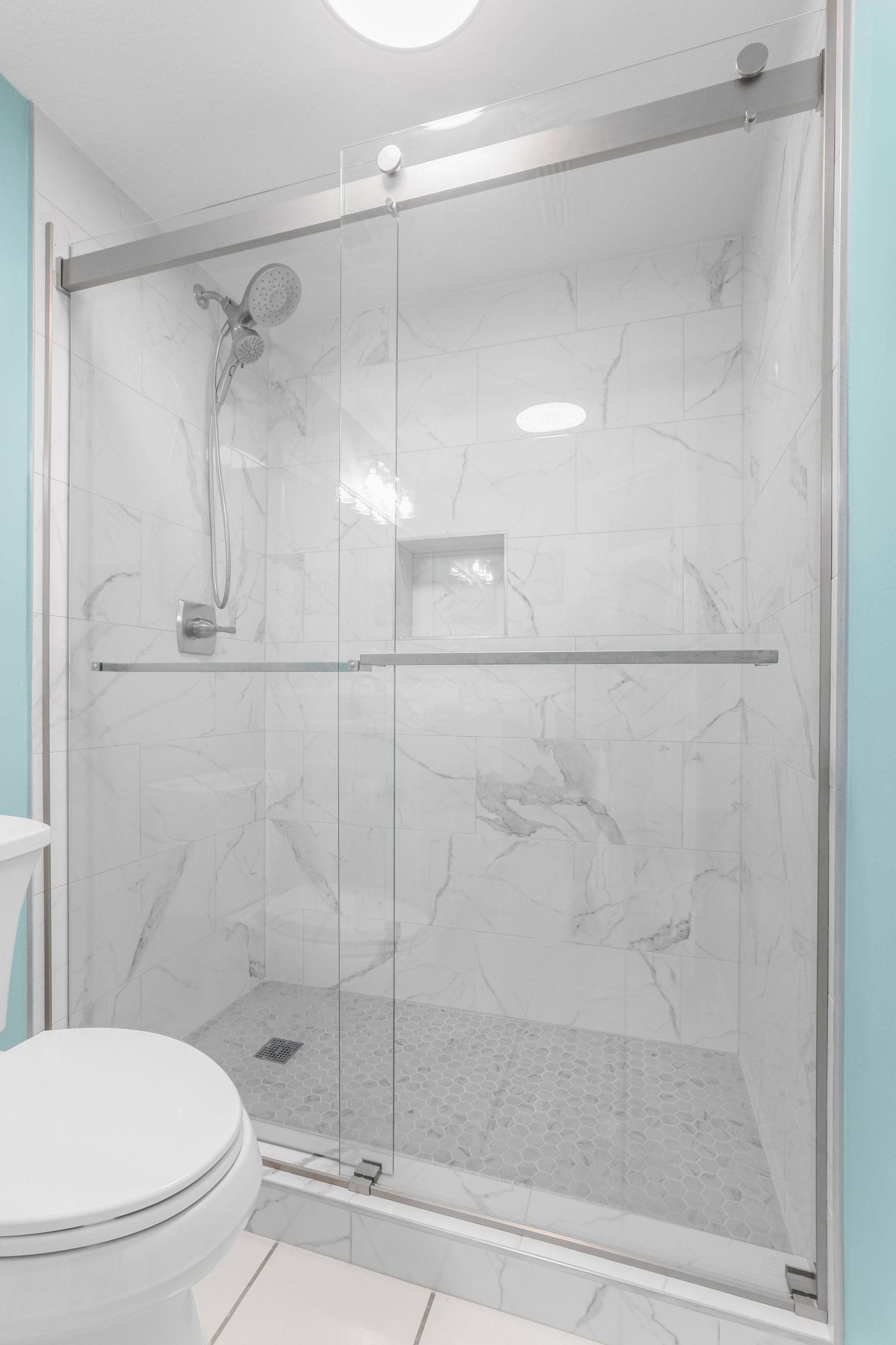 A modern bathroom with a glass-enclosed shower, a toilet, and a sink.