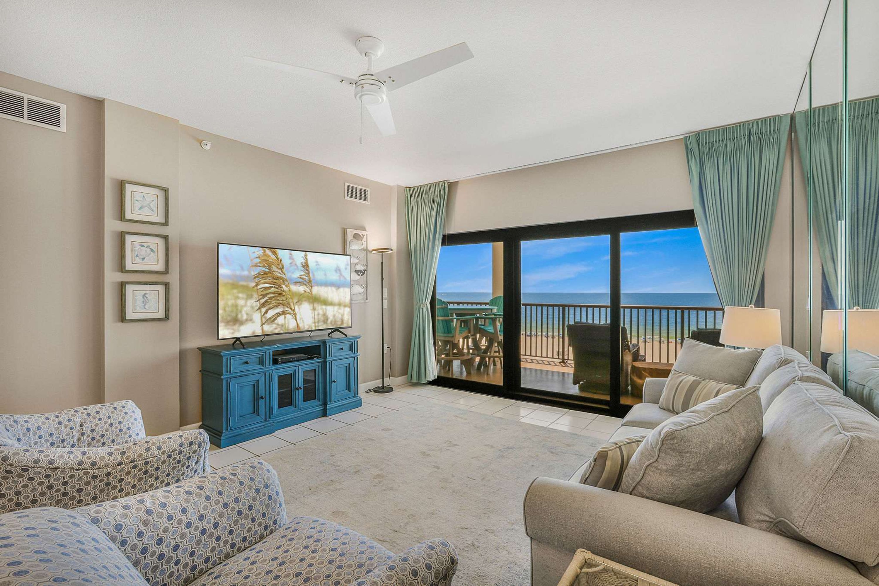 A living room with a large TV, blue cabinets, a beige sofa, and a balcony with a view.