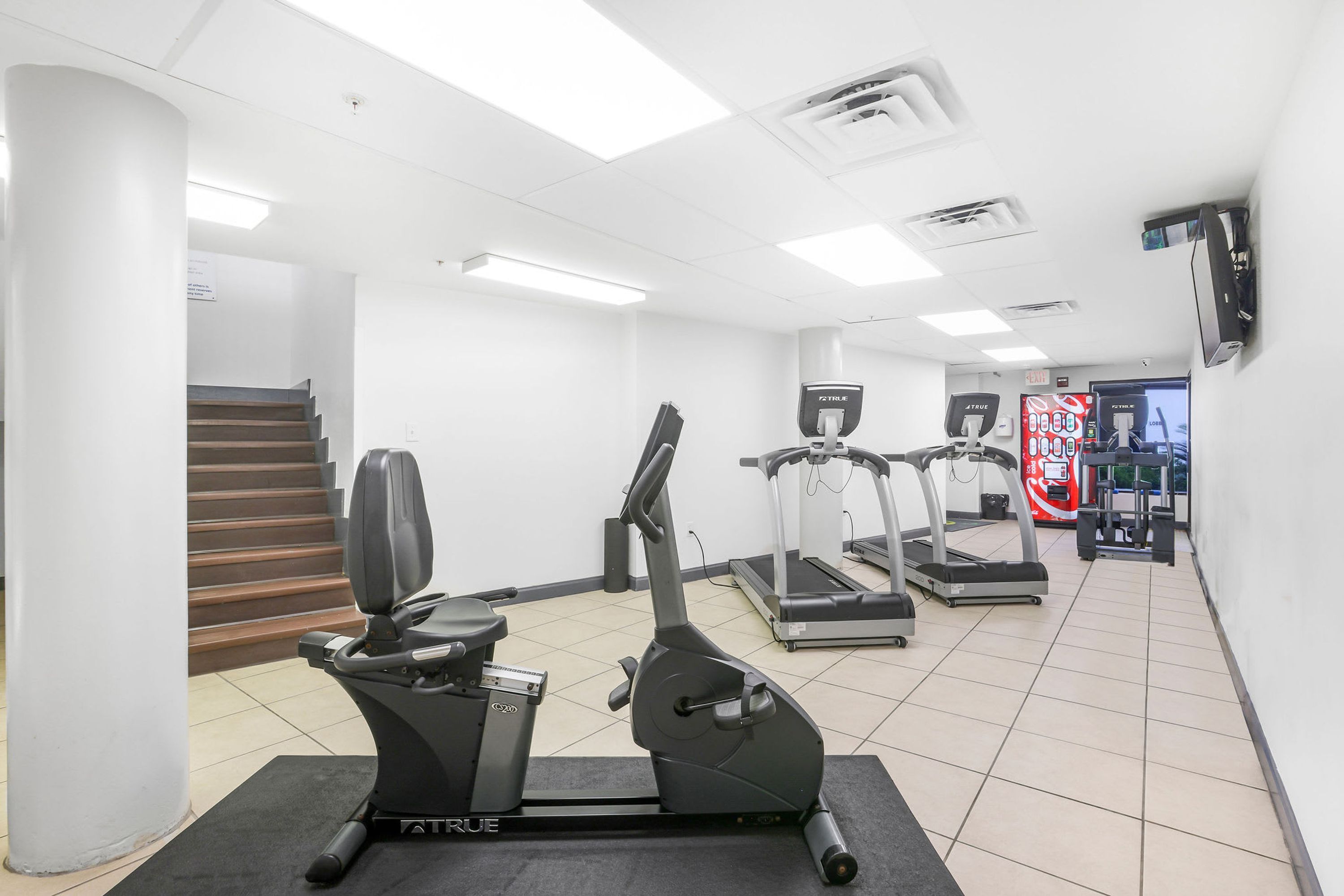 A gym with cardio machines, a treadmill, and a stairway.