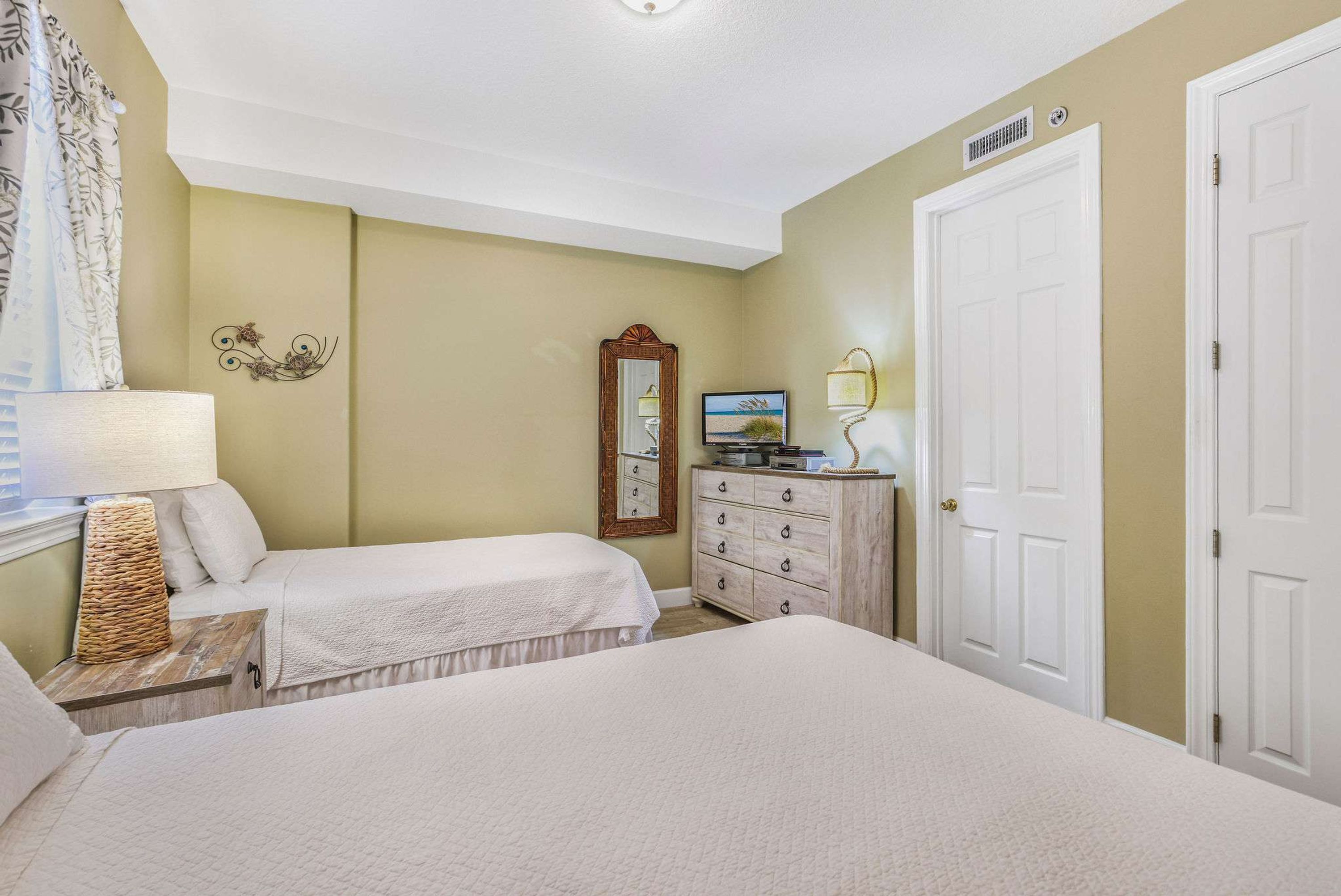 A bedroom with two beds, a dresser, a mirror, and a lamp.