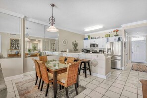 Een moderne keuken met een centraal eiland, een eethoek met rieten stoelen en een grote spiegel.