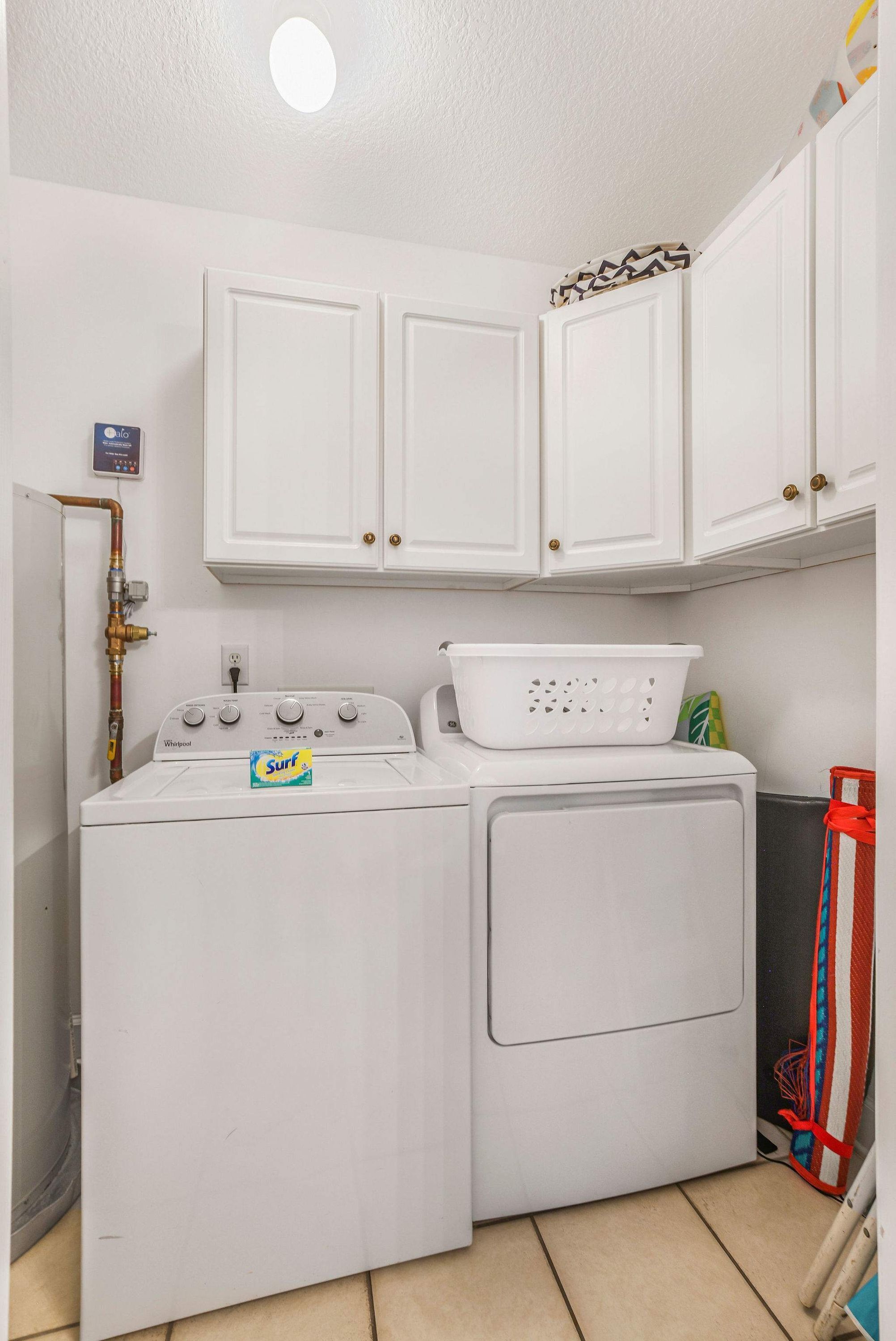 Un espace buanderie compact comprenant un lave-linge et un sèche-linge à chargement frontal, un meuble blanc au-dessus et un panier à linge sur le sèche-linge.