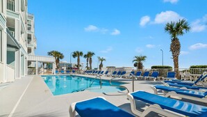 A pool area with blue lounge chairs and palm trees. - Grand Caribbean 111- Ground Level by Pool (Orange Beach)