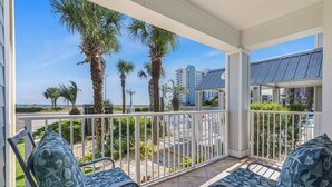 A balcony with two chairs and a table, overlooking a beach with palm trees and a cityscape in the background. - Grand Caribbean 111- Ground Level by Pool (Orange Beach)