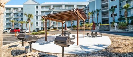 A covered outdoor area with barbecue grills, picnic tables, and a stone pathway.