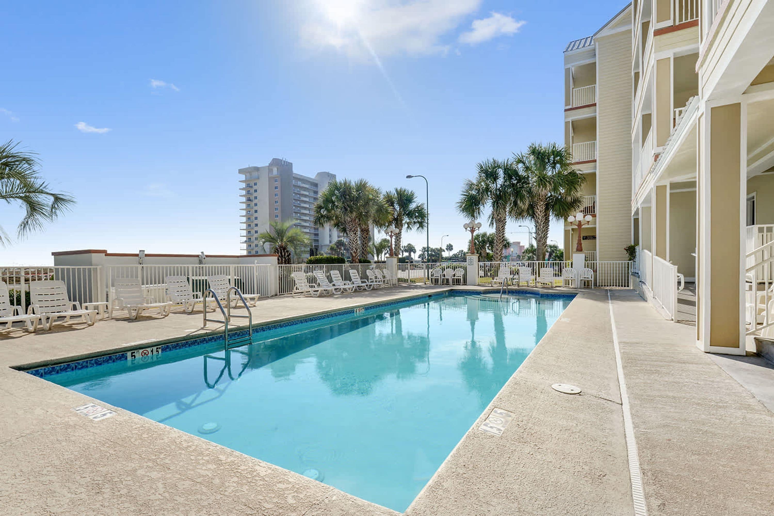 A rectangular pool with a tiled edge, surrounded by white lounge chairs and palm trees.