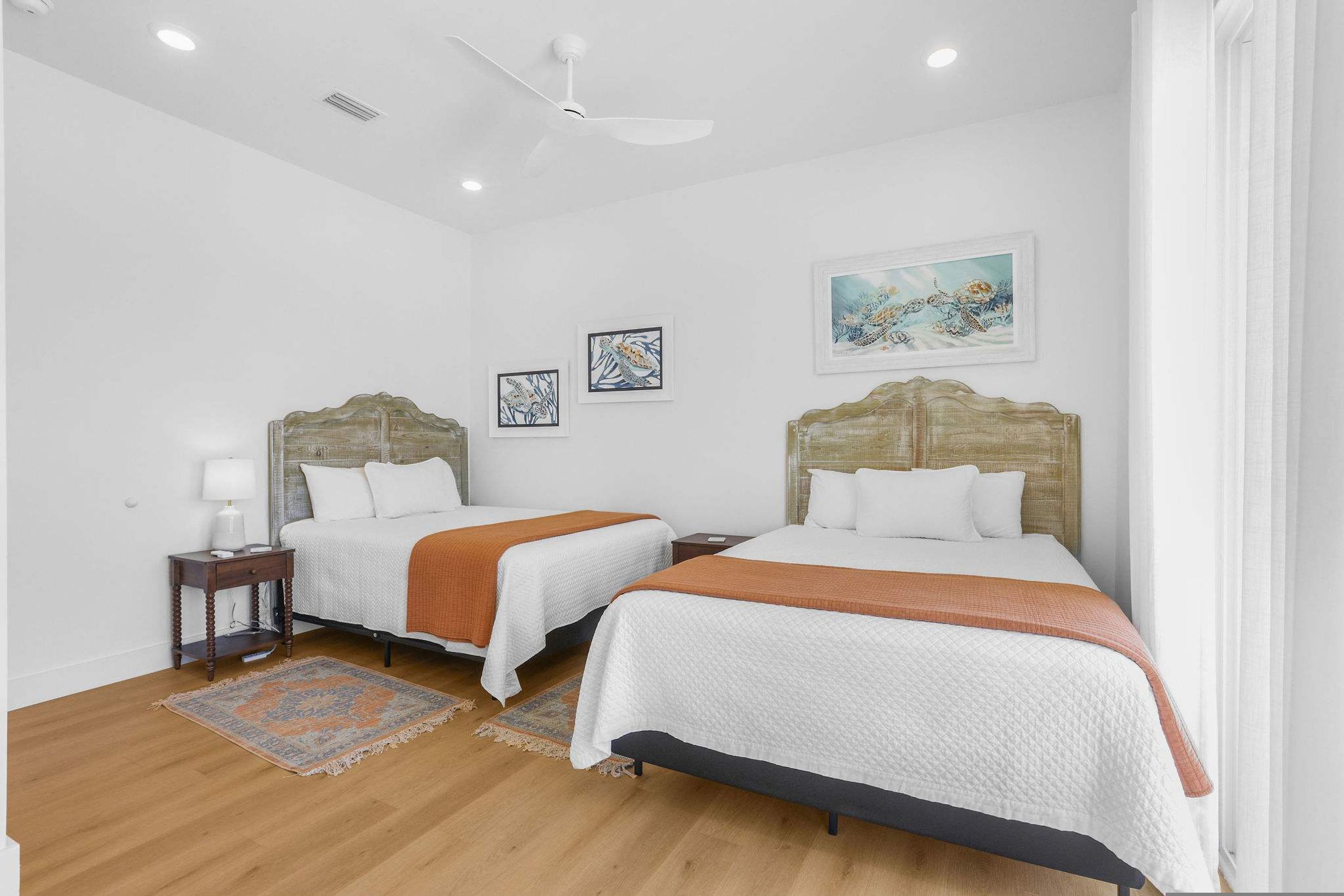 A hotel room with two beds, a ceiling fan, and artwork on the walls.