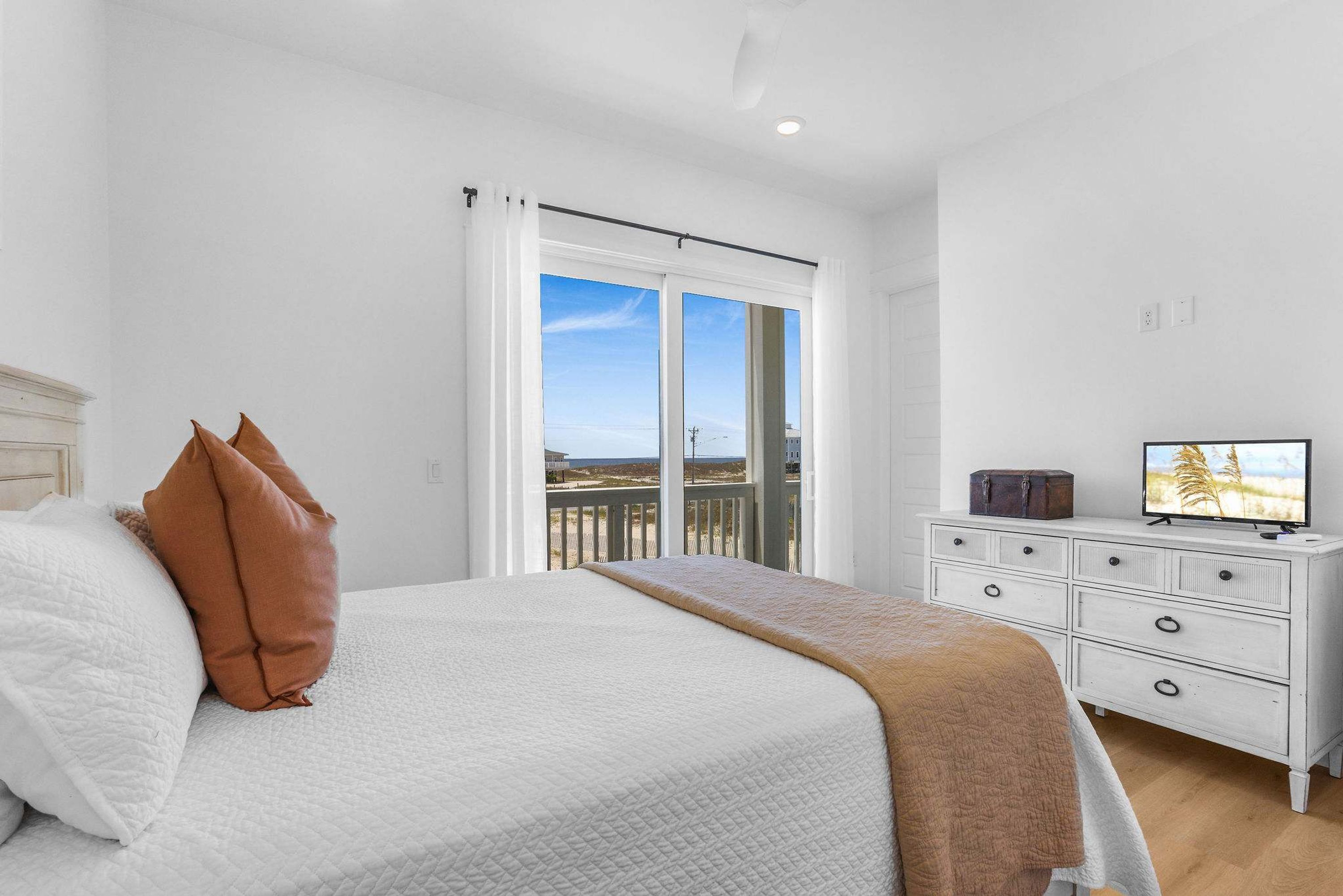 Une chambre à coucher avec un lit, des rideaux blancs, une commode et un téléviseur.