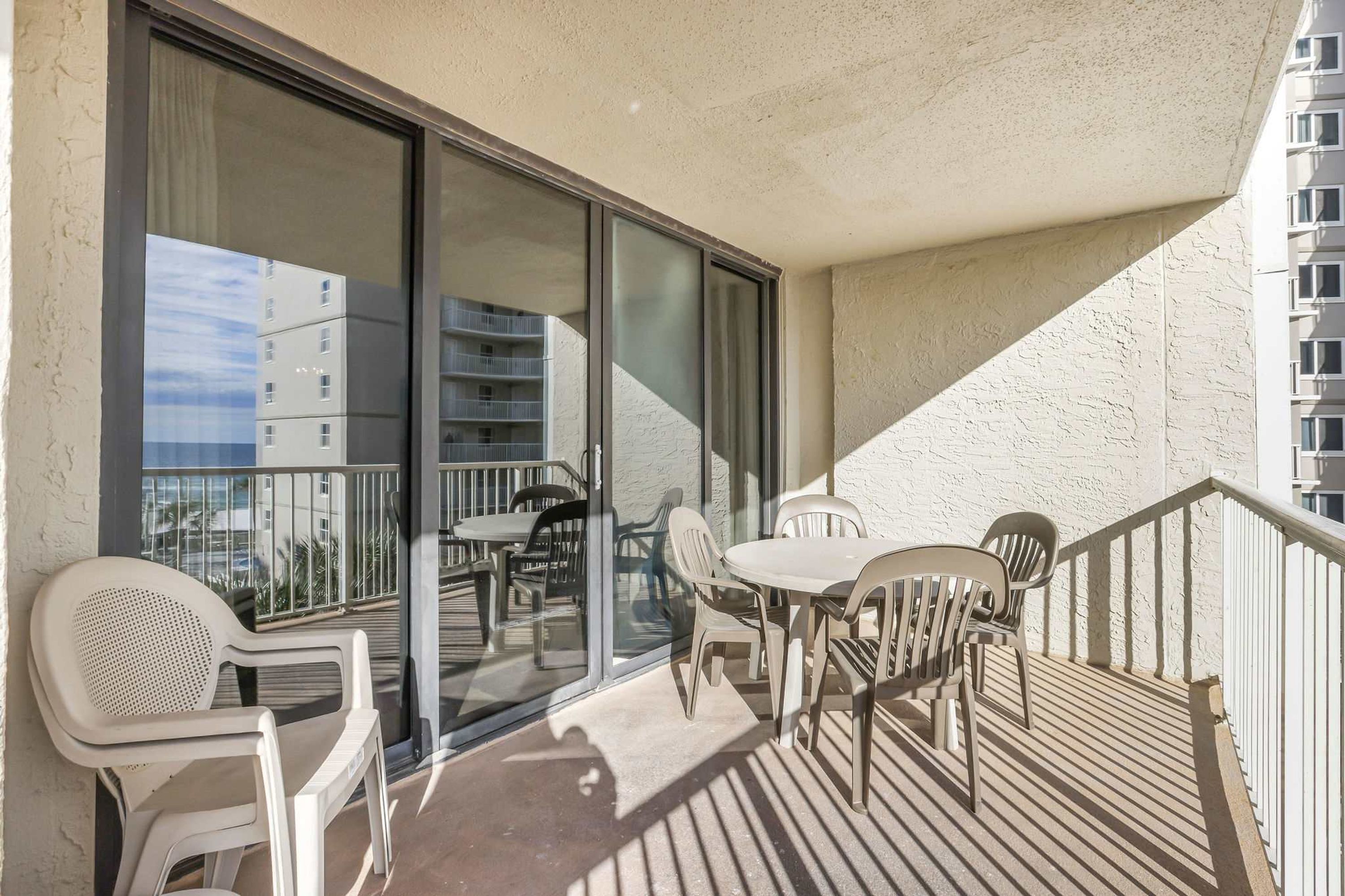 A balcony with plastic chairs and a table, large sliding glass doors, and a view of other buildings.
