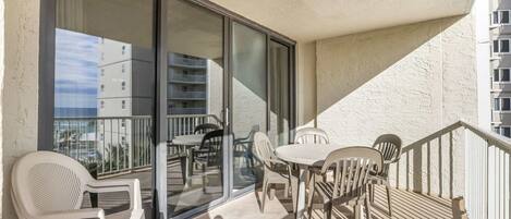 A balcony with plastic chairs and a table, large sliding glass doors, and a view of other buildings.