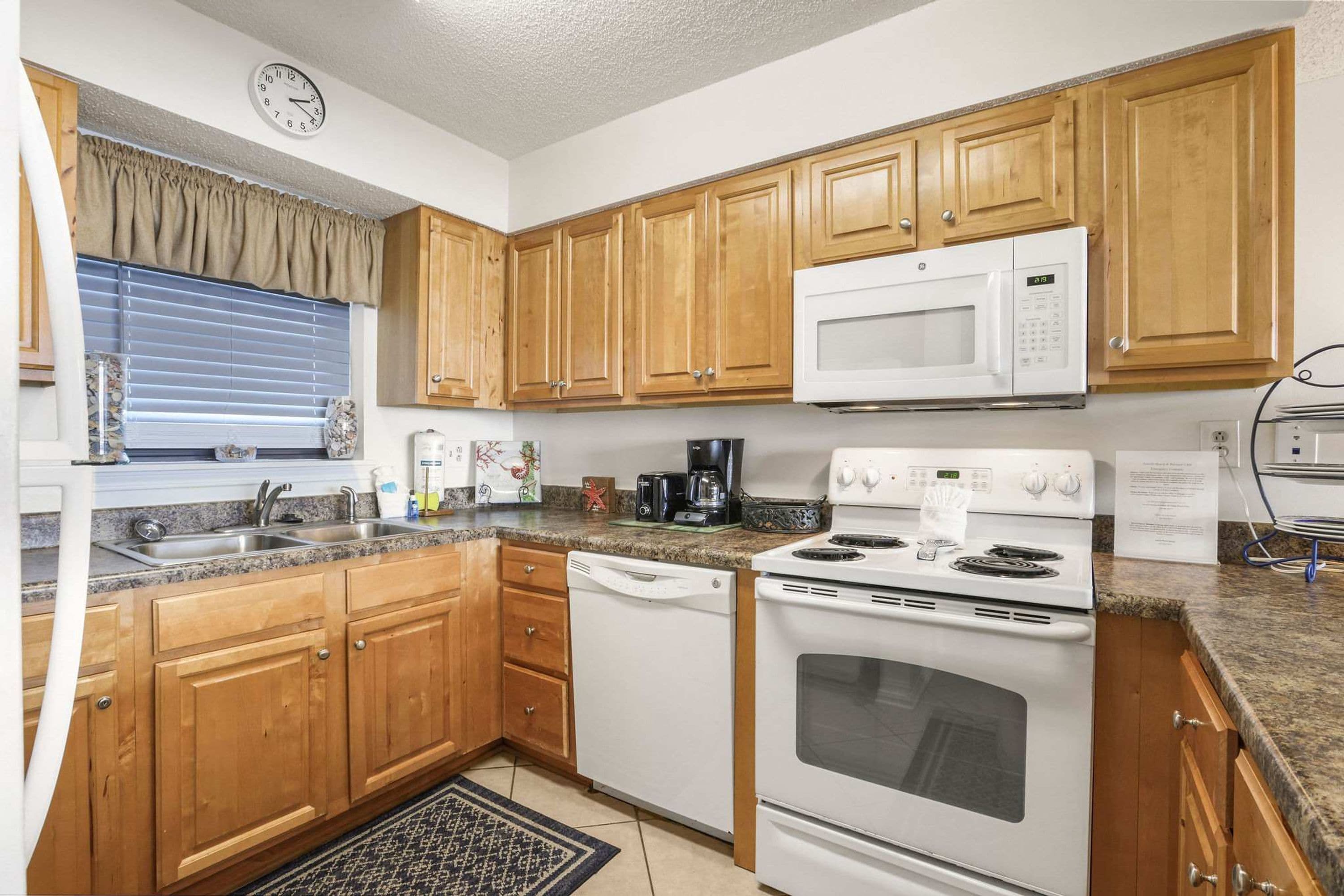 A kitchen with wooden cabinets, a microwave, a stove, a dishwasher, and a clock on the wall.
