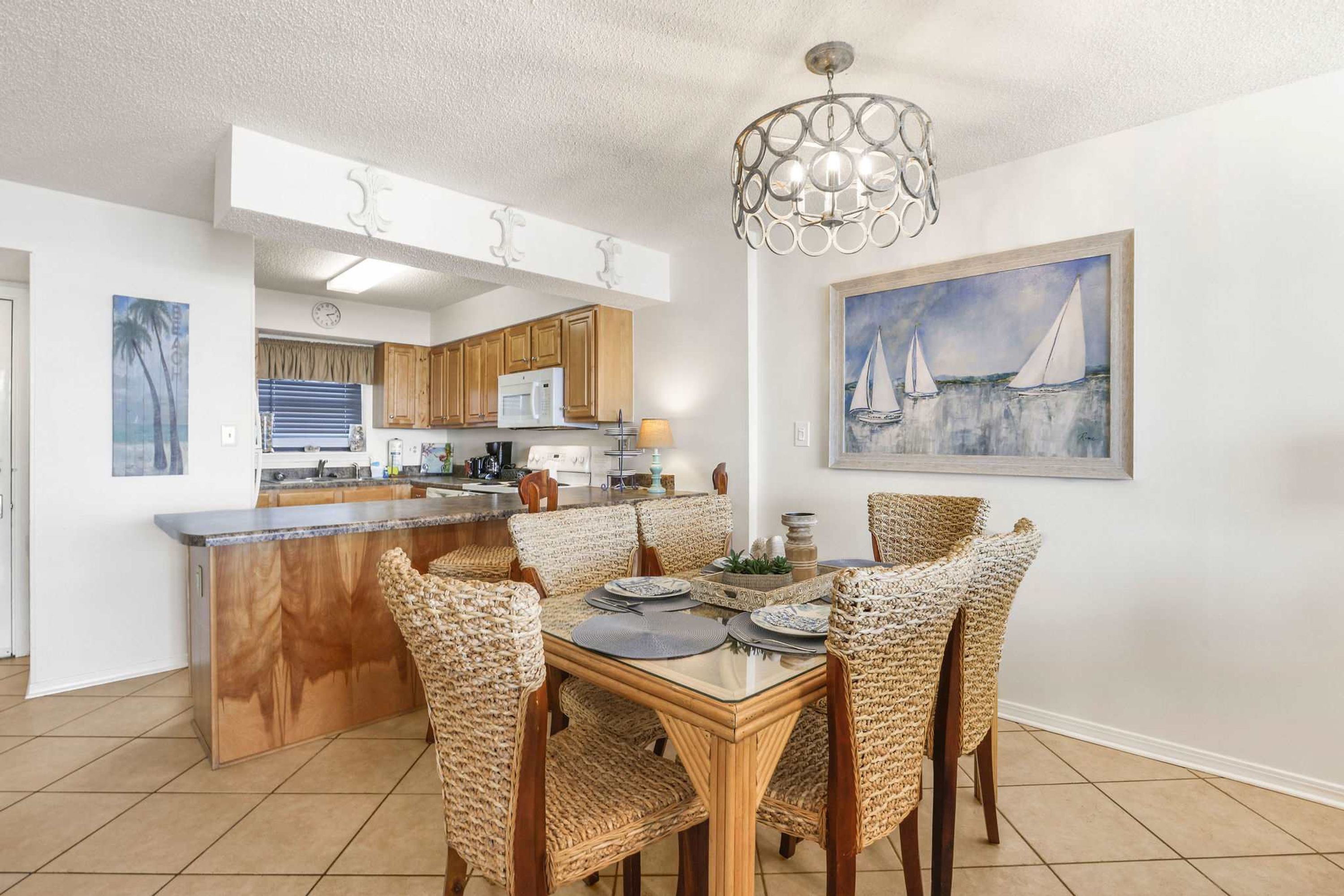 A dining area with a central island, wicker chairs, and a painting of sailboats on the wall.