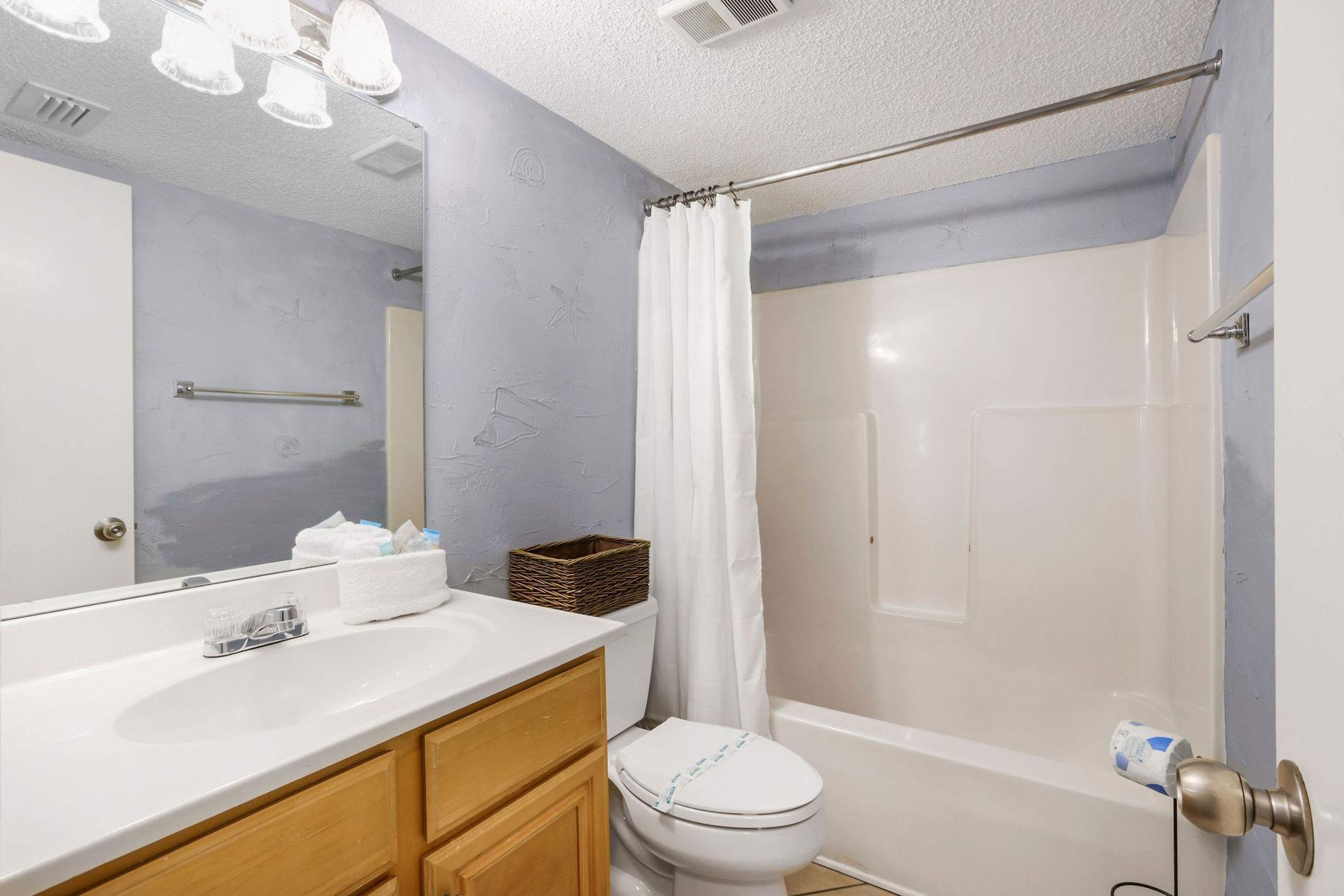 A bathroom with a white sink, wooden cabinets, a white toilet, a shower curtain, and a bathtub.