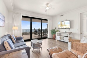 A spacious living area with a balcony, a sofa, a coffee table, a TV, and a plant. - Grand Pointe 512 Gulf-front Stunning Views Top-notch Amenities 2 Bedrooms 5th Floor (Orange Beach)