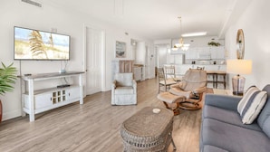 A spacious living room with a television, seating area, and a kitchen in the background. - Grand Pointe 512 Gulf-front Stunning Views Top-notch Amenities 2 Bedrooms 5th Floor (Orange Beach)