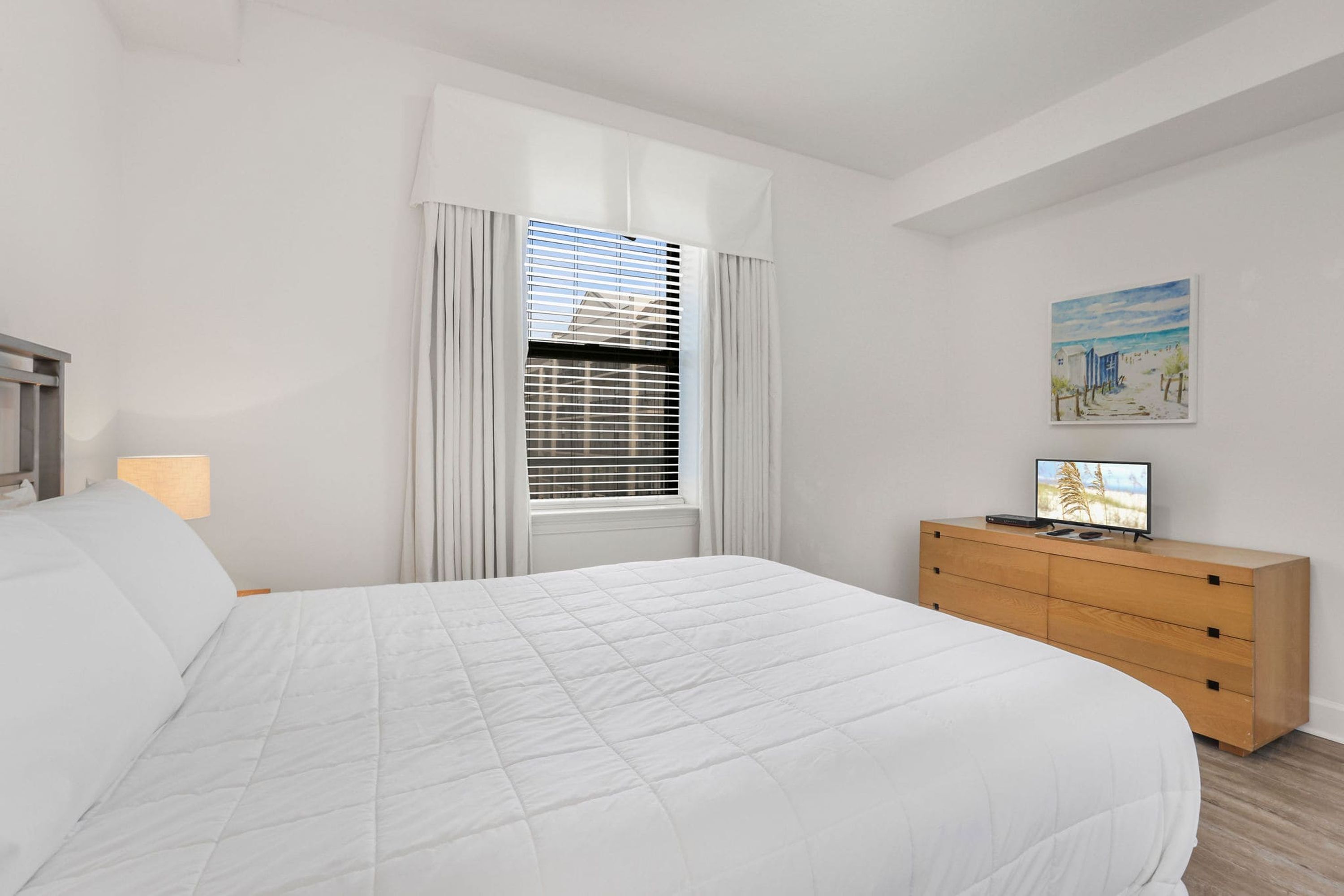 A bedroom with a bed, a dresser, a window with curtains, and a painting on the wall.
