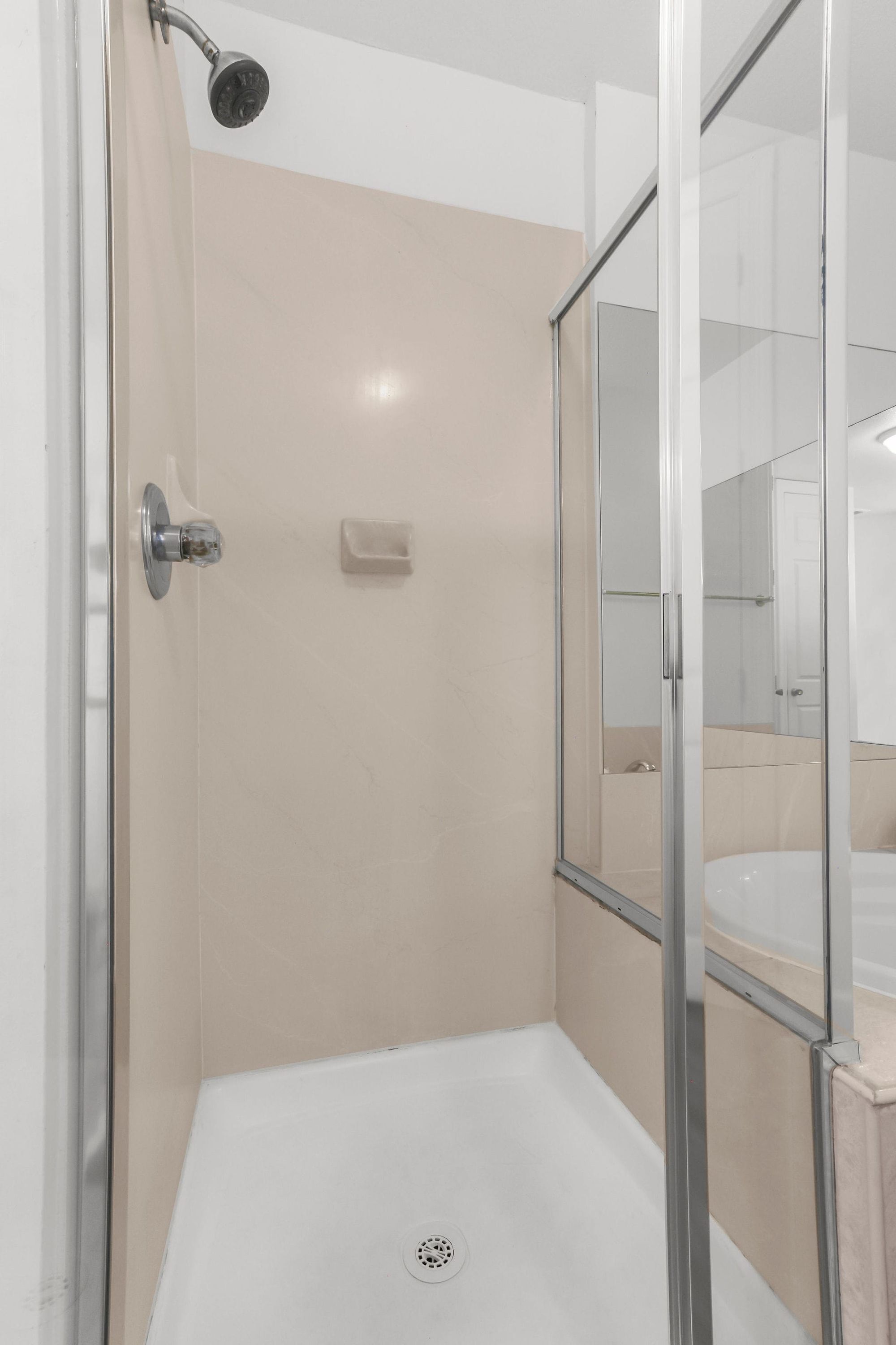 A walk-in shower with a glass door, a white tiled wall, and a visible drain.