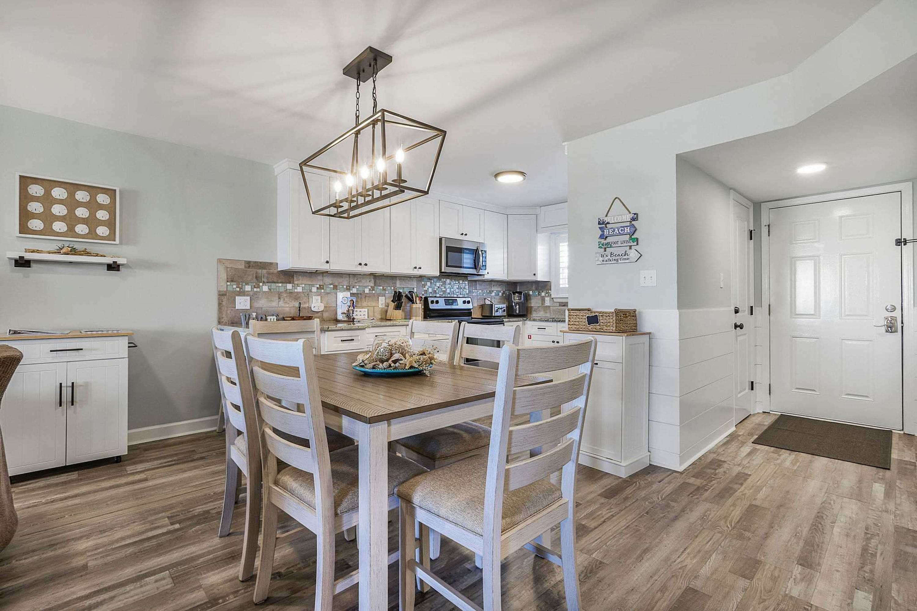 Une cuisine moderne avec des meubles blancs, une table à manger en bois et un lustre.