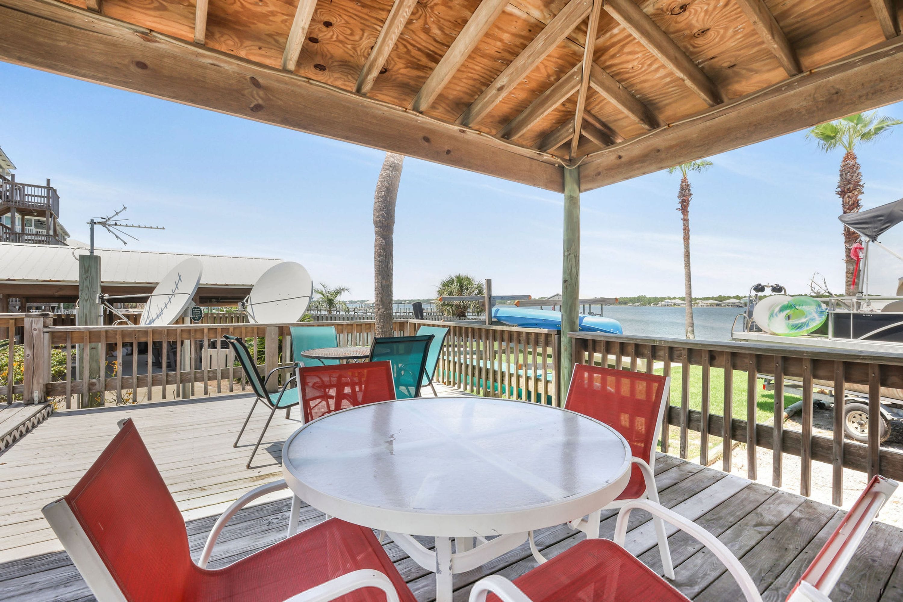 A covered outdoor area with a wooden deck, a round table, and red and white chairs.