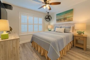 A bedroom with a bed, a ceiling fan, a window with blinds, a wall-mounted artwork, and a nightstand with a lamp. - Gulf Shores Getaway Lagoon Front Beach Access Family Fun Lagoon Landing 202 (Gulf Shores)