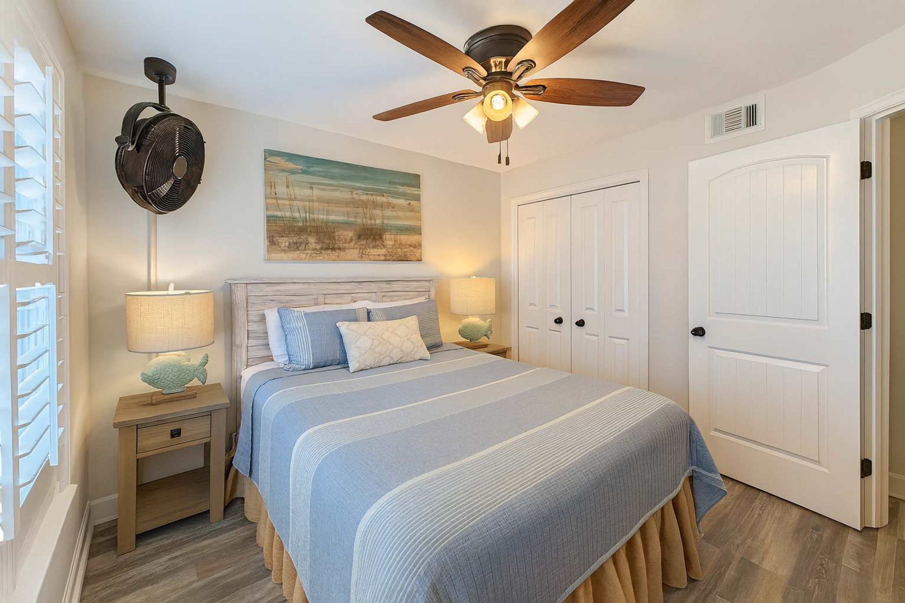 A bedroom with a bed, two bedside tables, a ceiling fan, and a door.