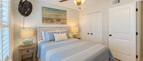 A bedroom with a bed, two bedside tables, a ceiling fan, and a door.