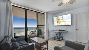 A modern living room with a sofa, a coffee table, a TV, and a balcony with a view of the beach. - Seaside Beach 3902- 2 BR Direct Beachfront Condo With Pool Sauna Amazing Ocean View Balcony (Orange Beach)