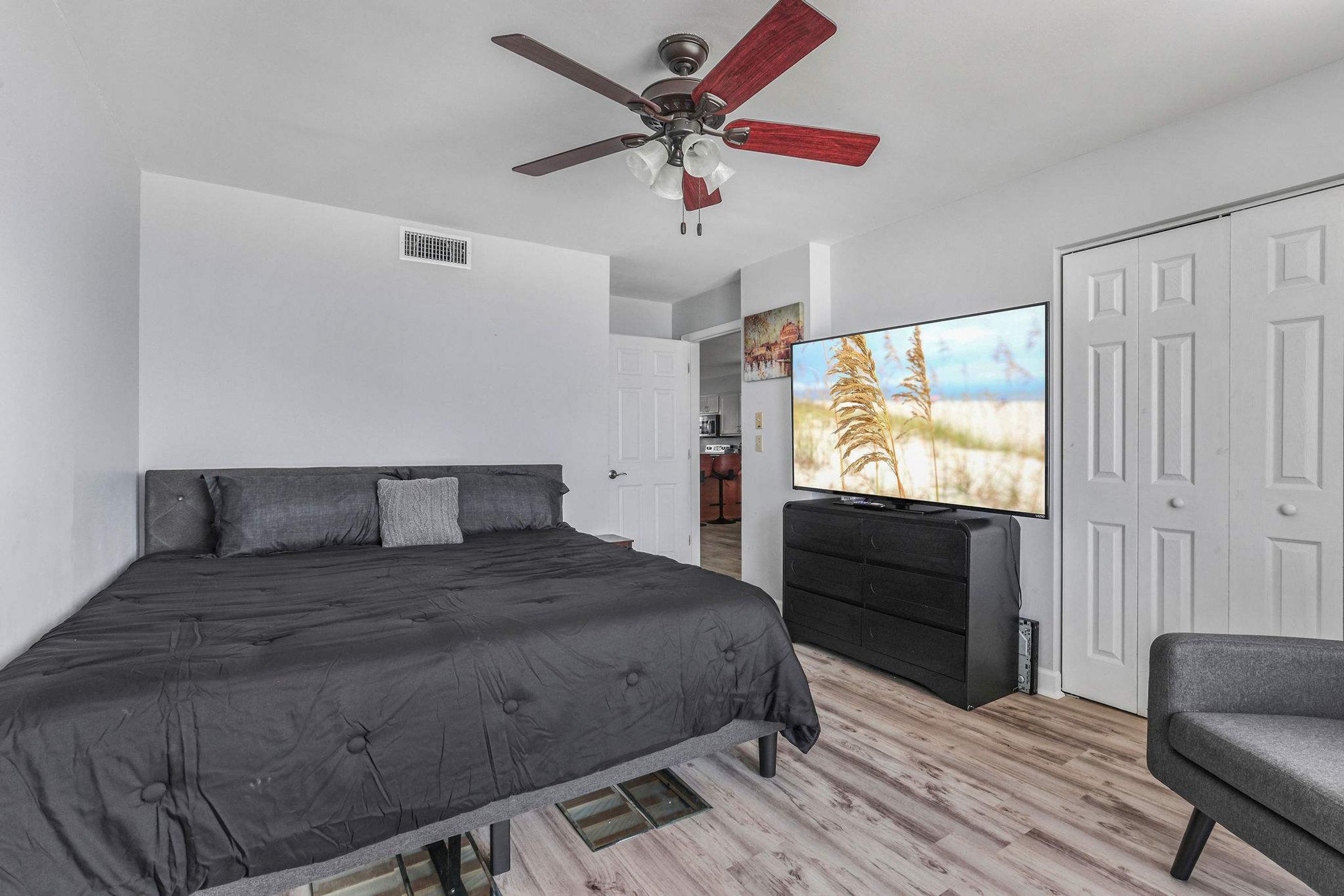 Une chambre à coucher comprenant un lit, un téléviseur, un ventilateur de plafond et une armoire.