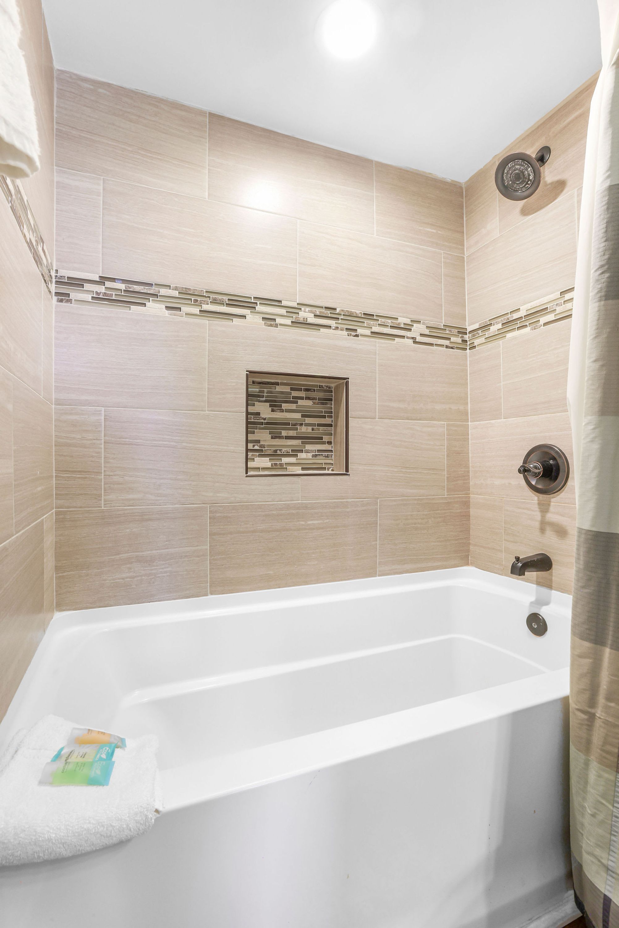 A bathroom with a bathtub, tiled walls, a showerhead, and a towel rack.