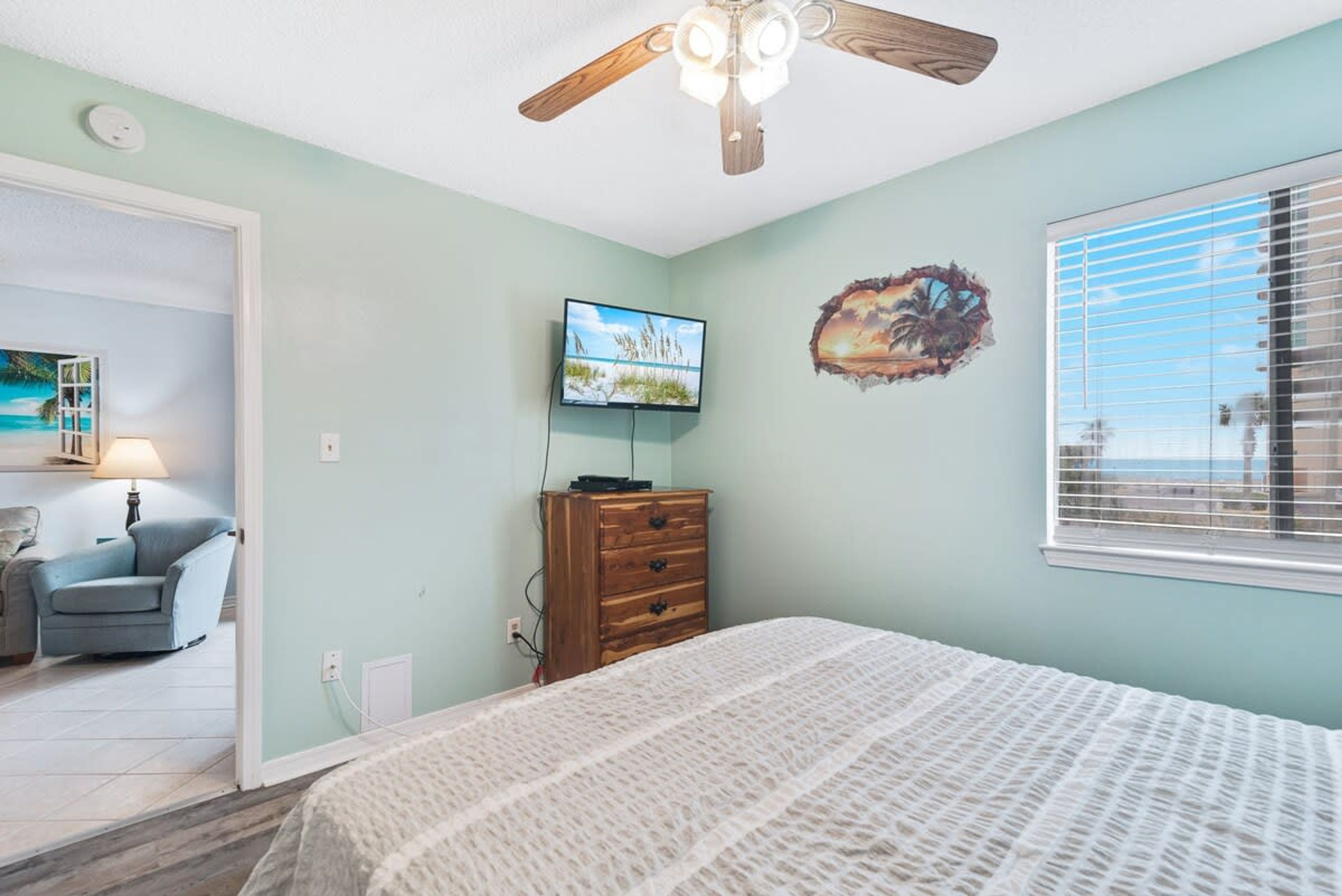 Un dormitorio con cama, ventilador de techo, televisión y ventana con persianas.