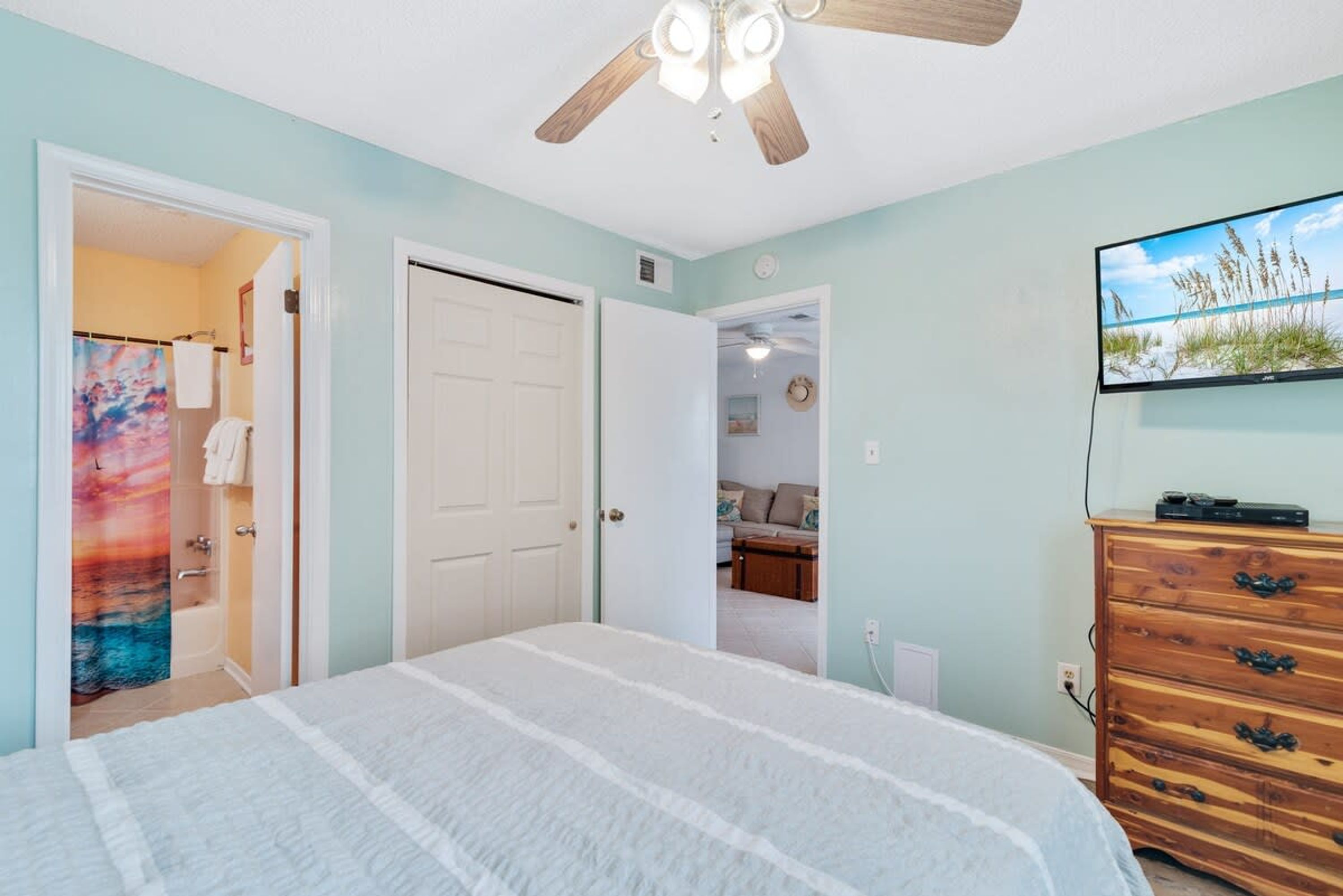 A bedroom with a bed, a ceiling fan, a dresser, and a TV on the wall.