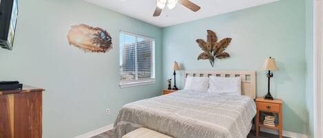 A bedroom with a bed, a ceiling fan, a window, and a wall-mounted TV.