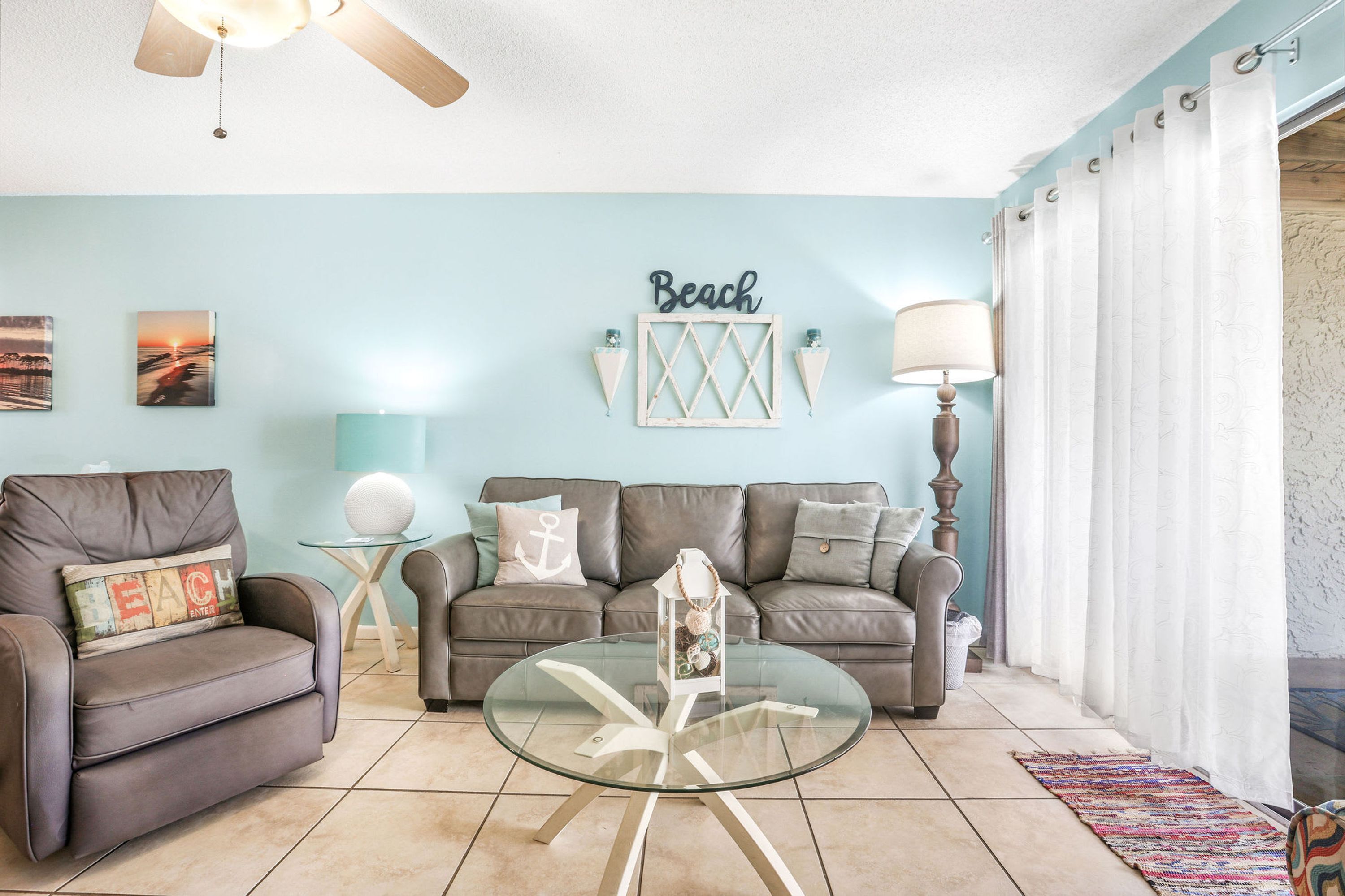 A living room with a blue wall, a glass coffee table, a sofa, and a ceiling fan.