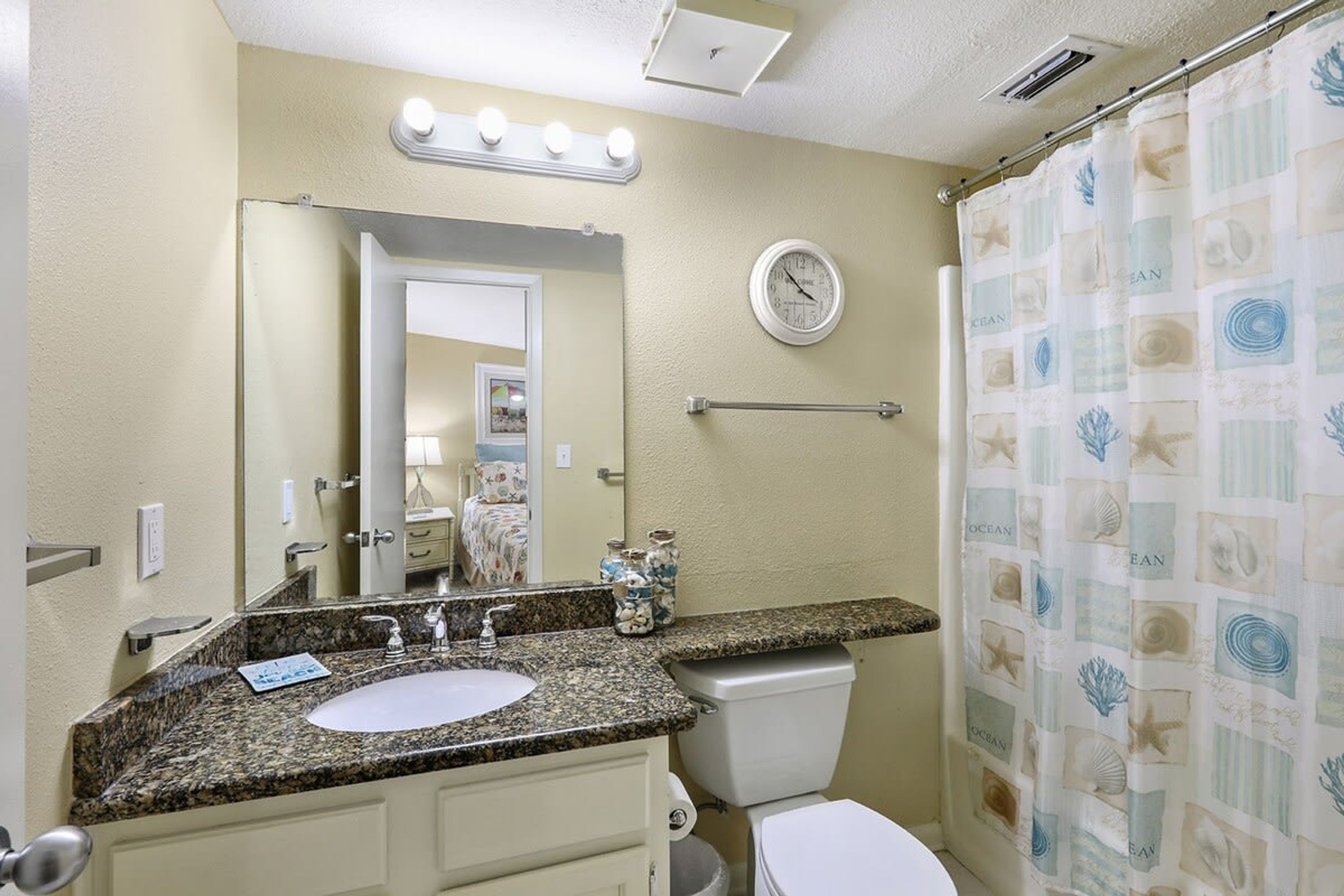 A bathroom with a sink, mirror, vanity, toilet, and shower curtain.