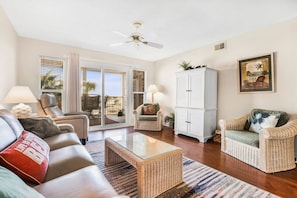 A spacious living room with a glass coffee table, leather sofas, wicker armchairs, and a white cabinet. - Portside 204- Best of Beach Bay (Orange Beach)