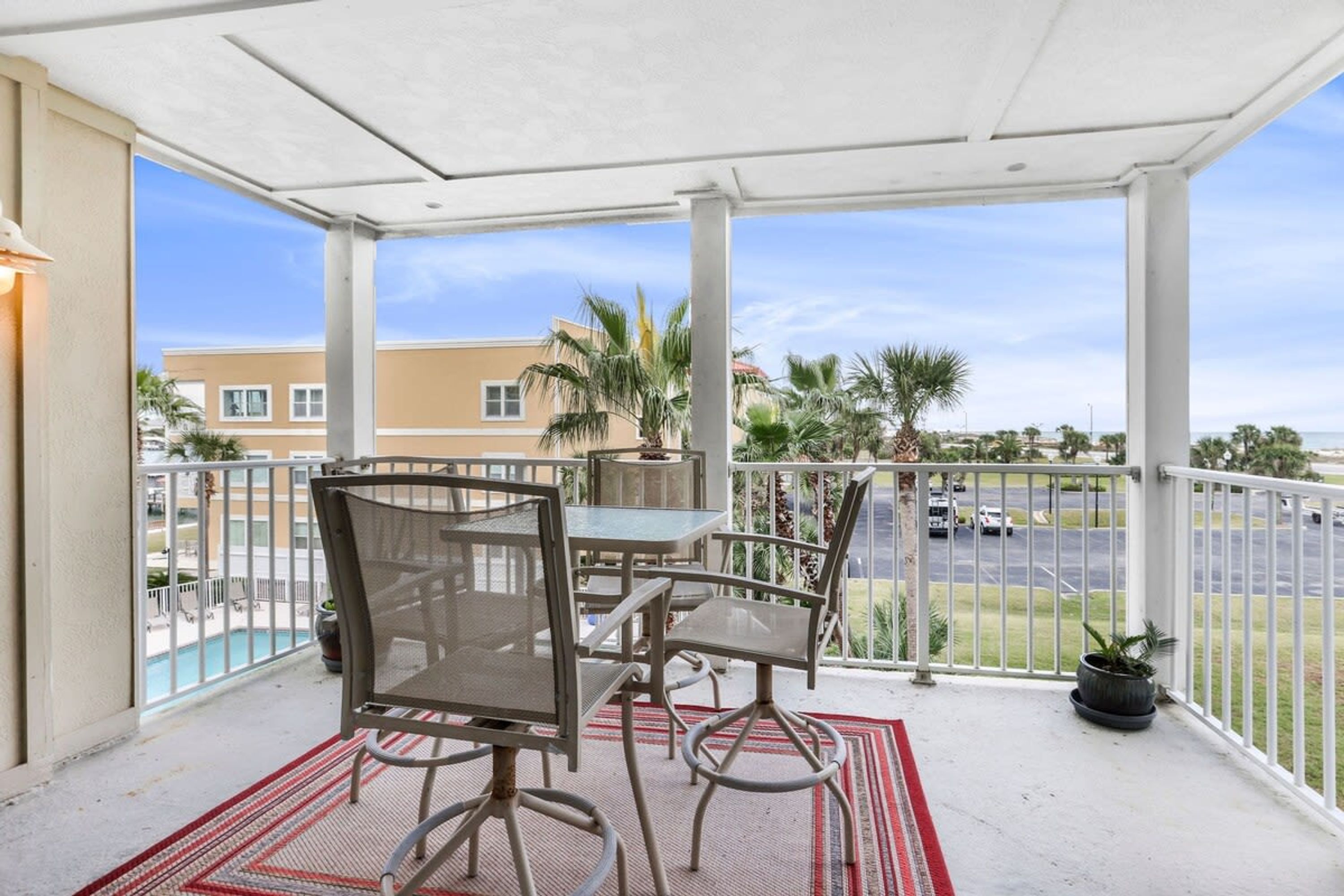 Un balcone coperto con mobili da esterno, vista sulla piscina e un'area parcheggio.