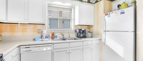 A kitchen with white cabinets, a window with blinds, a sink, a stove, and a refrigerator.