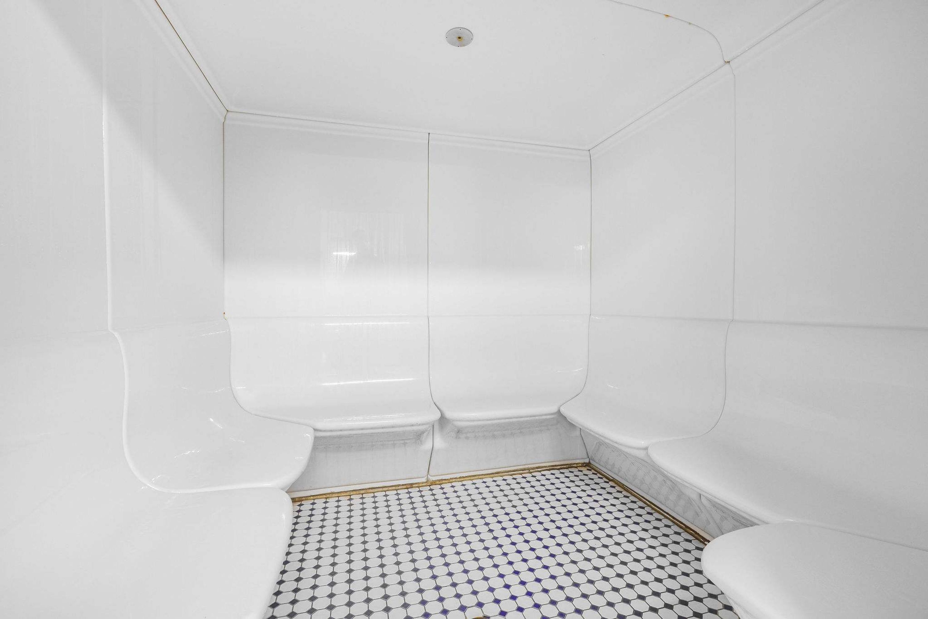 A bathroom with white walls, a tiled floor, and a shower area.