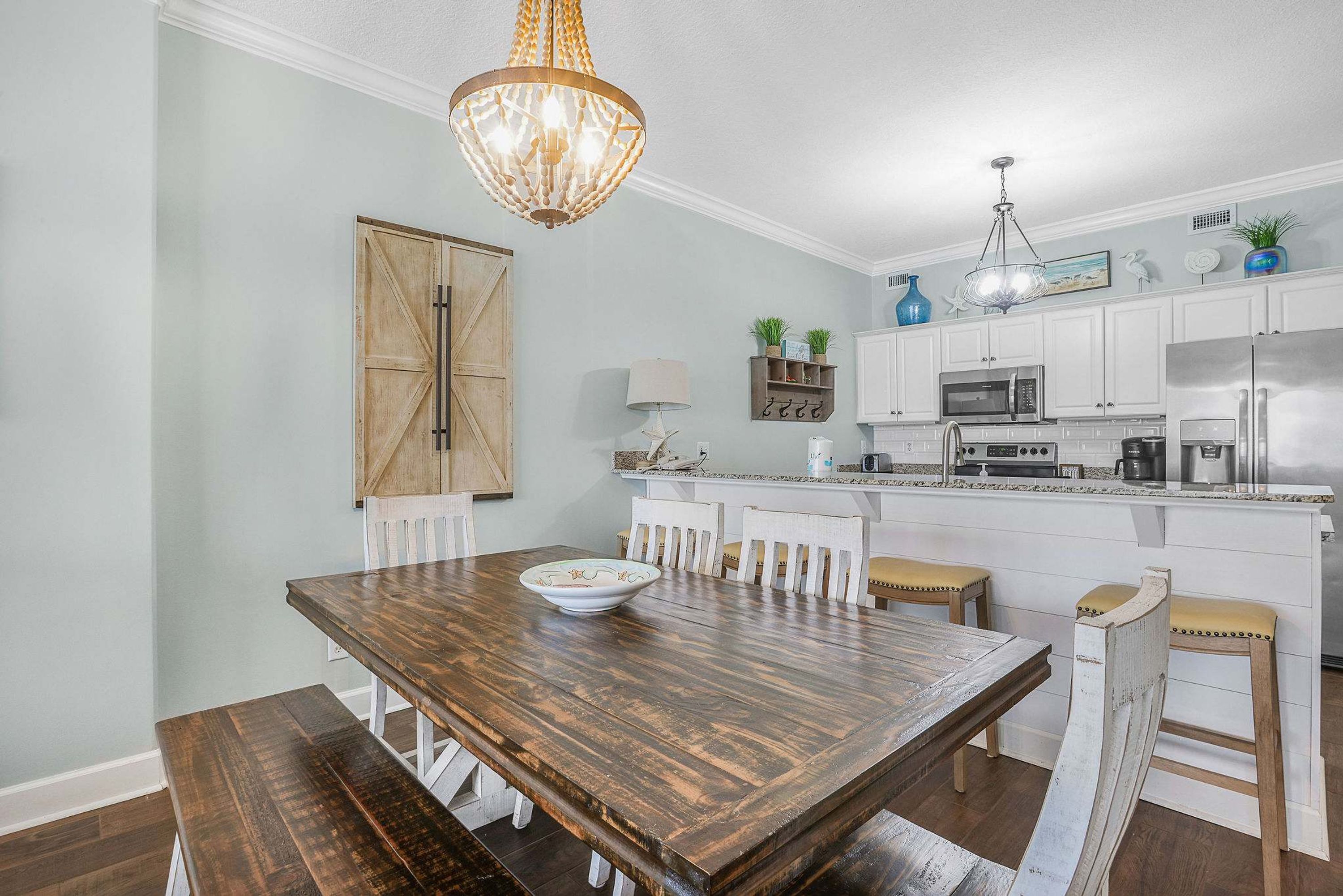 A dining area with a wooden table and benches, a chandelier, and white cabinetry in the background.
