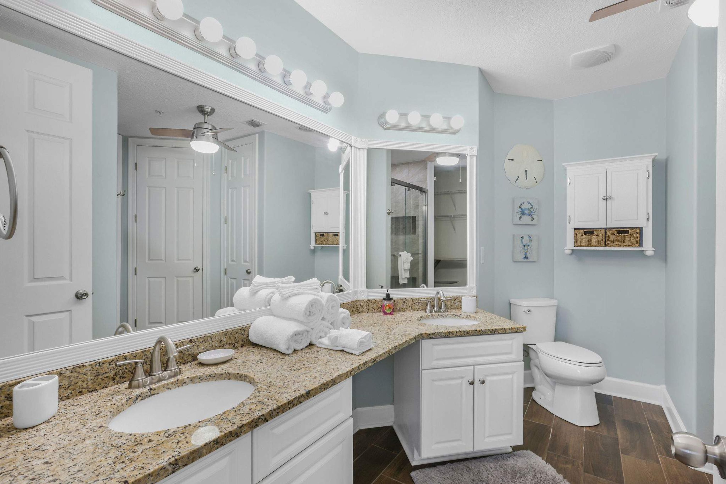A bathroom with a large vanity, a sink, a mirror with lights, a toilet, and a shower area.