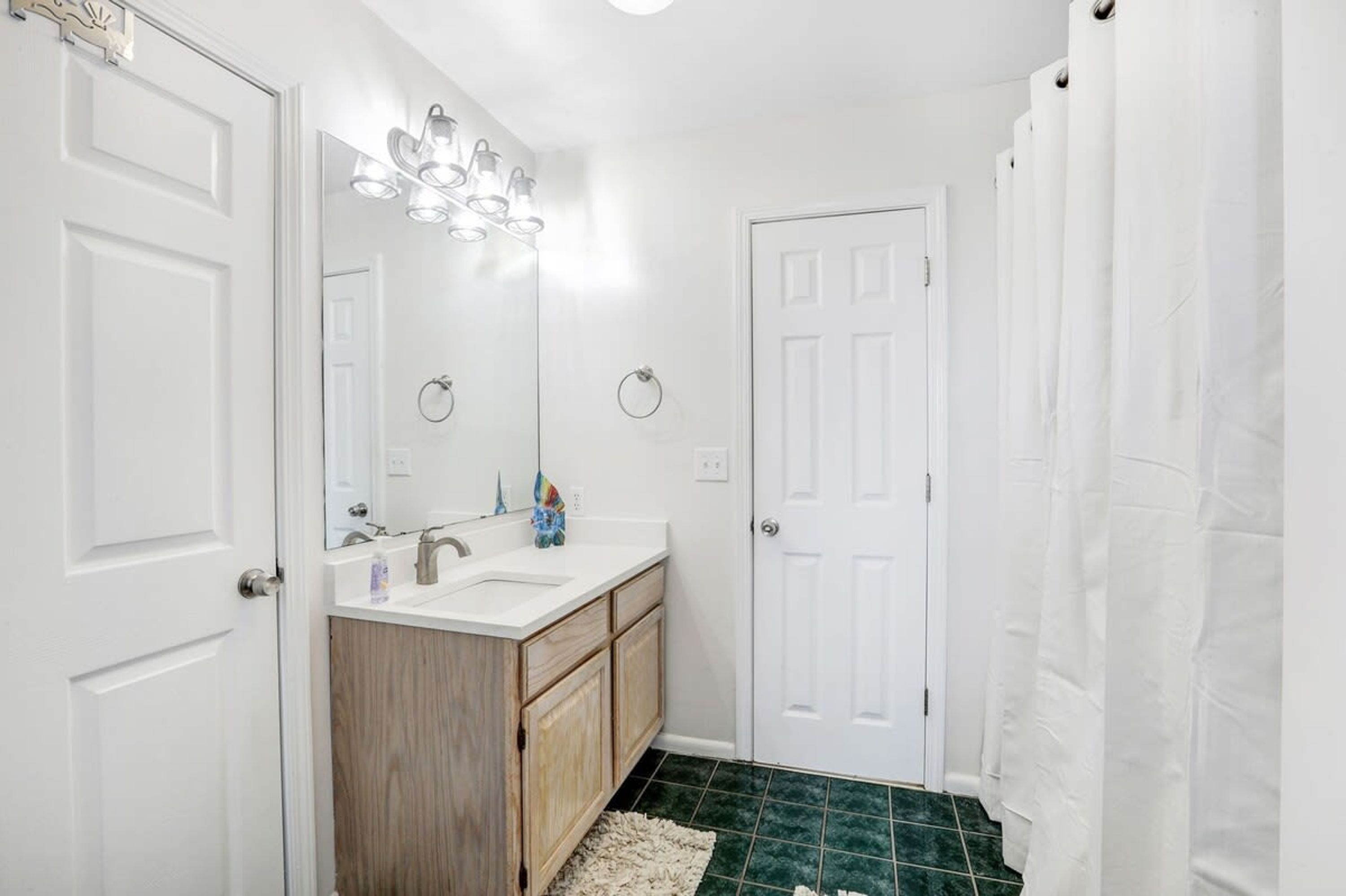 A bathroom with a white vanity, a mirror, a sink, and a shower curtain.
